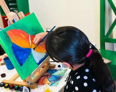 الرسم من مرجع — فراشة على خلفية خضراء، والصورة المرجعية أمام الطالبة